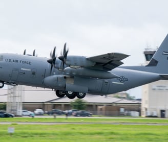 US Air Force Hurricane Hunter plane taking off with ground just below plane and control tower in back ground.