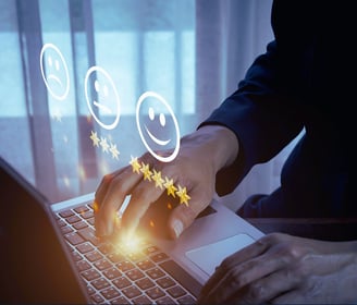 A leader types on a laptop as holographic sad, neutral, and happy faces appear to measure customer satisfaction, face unseen.