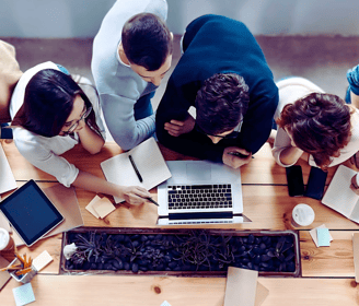 A group of leaders huddle around a laptop at a table, discussing the content on the screen.