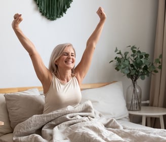 a woman in a white tank top and a white bed with a blanket