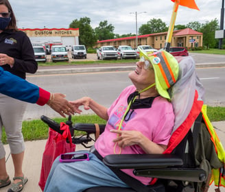 Photo of Dawn Zuterberg sitting in her electronic scooter, shaking someone's hand