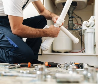 A plumber in a white shirt is holding pipes to fix a sink.