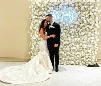 Newlyweds taking a photo in front of the white rose flower wall during their wedding