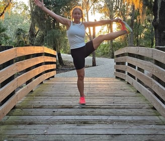Eva practicing balance yoga pose on a wooden bridge at sunset, surrounded by nature.