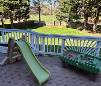 Photo of outdoor play area with sand pit and green slide.