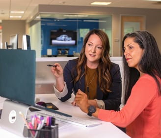 two women sitting at a desk with a laptop