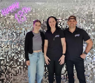 Laura with Carly and Kahn from Sweetaz Co. in front of a silver shimmer wall with a Happy 18th neon sign.
