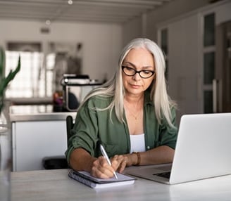 a woman in glasses and a green shirt is sitting at a desk with a notebook