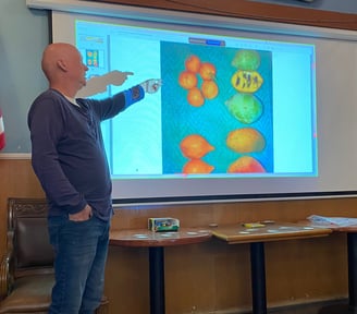 Man standing in front of a slide showing pawpaws and other fruit for size comparison