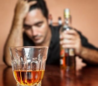 homme 1 bouteille d'alcool à la main gauche main droite sur la tête et verre devant lui presque vide