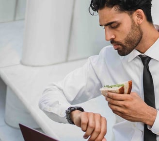 a man at office eating sandwich while looking at time