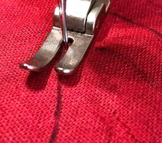 Gros plan sur le pied presseur d'une machine à coudre suivant des lignes sur un tissu