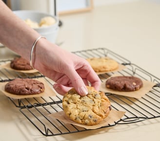 A hand picks up a freshly baked vanilla choc chip cookie.