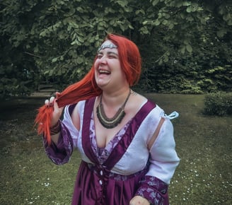 Femme rousse riante et joyeuse dans une robe violette et blanche dans un fond verdoyant