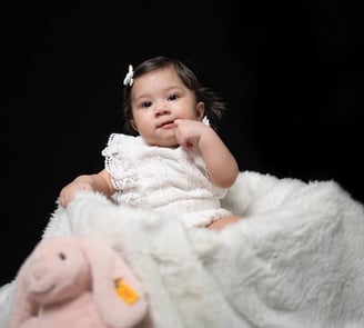 a baby girl sitting on a blanket with a pink stuffed animal