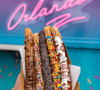 a person holding a box of donuts with chocolate and sprinkles