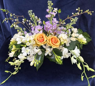 Aranjament cu trandafiri galbeni, flori albe și mov pe fundal albastru.