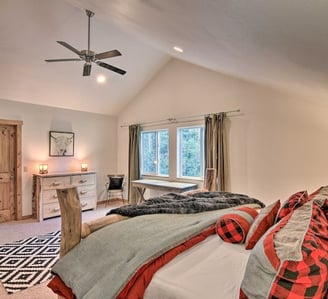 Large bedroom with mountain view window, desk, and cozy red-accented bed.