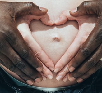 mains d'un ouple interracial  sur le ventre de la femme enceinte et  formant un cœur