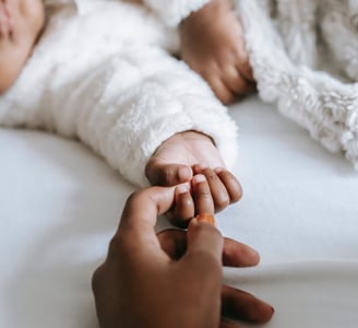 Maman qui tient la main de son bébé qui dort sur un lit - Micro-crèche et crèche différence
