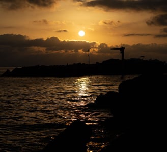 Silhouette of a rocky - shoreline shimmering reflection of the setting sun on the water - Bogliasco