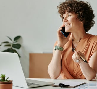 a woman sitting at a desk with a laptop and talking on a cell phone