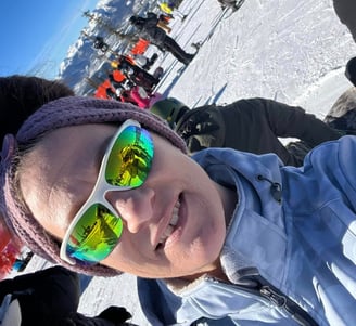 a woman in sunglasses and a hat skiing on a sunny day