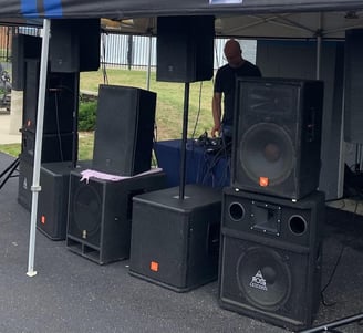 man under a tent behind speakers playing music