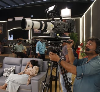 a man is filming a video camera and a woman is sitting on a couch