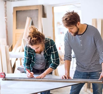 Une femme et un homme en train de mesurer une planche de bois