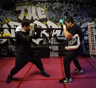 a man is training with his coach in a boxing ring with boxing gloves and pads