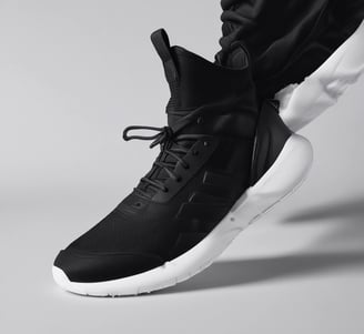 A single sports shoe is prominently displayed against a seamless, light turquoise background. The shoe features a sleek design with a gradient of light gray to dark gray tones, and is equipped with a distinctive CloudTec sole for cushioning. The branding logo is subtly visible on the side.