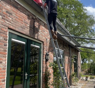 Man op ladder die dakgoot leegmaakt tijdens dakgootreiniging in Groningen