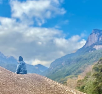 raveler sitting on a mountaintop gazing toward distant volcanic peaks beneath a blue sky in Japan