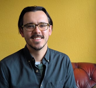 Tom King smiling towards the camera, with a yellow background.