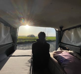 Person sitzt entspannt im selbst ausgebauten Dacia Dokker Camper, mit geöffneter Hecktür und Blick i