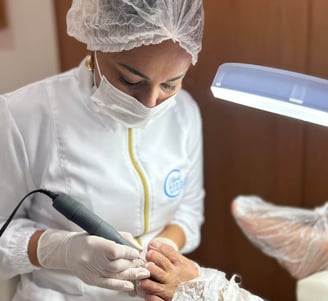 Uma profissional de podologia, vestida com touca descartável, máscara e jaleco branco com detalhes em amarelo