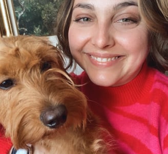 a woman in a hot pink sweater holding a golden doodle puppy with art in the background in portland
