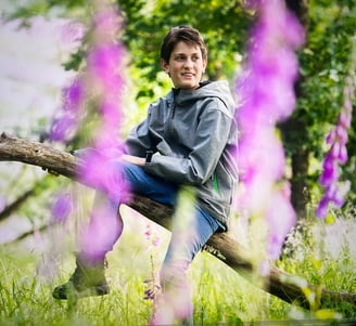 Der junge Naturfotograf Philipp Geisler sitzt auf einem Ast, im Vordergrund Wildblumenblüten