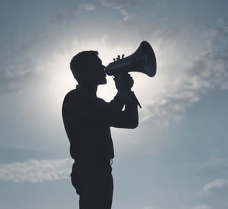A silhouette of a person holding a megaphone against a clear blue sky, suggesting communication or a call to action.