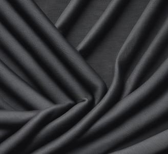 A close-up view of a denim fabric with prominent stitching details. A small red tag with black text is visible, partially showing a brand name. The fabric texture and stitching are clearly defined, illustrating the quality and craftsmanship of the material.