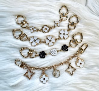 Gold-toned chain accessories featuring heart-shaped links and enamel flower charms in white and blac