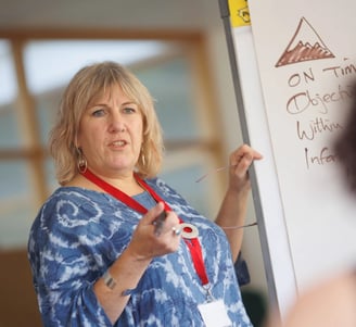 a woman in a blue dress is standing in front of a white board