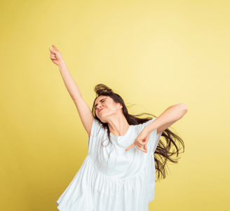 L'immagine mostra una donna che indossa una blusa bianca, posando con un'espressione energica e gioiosa su uno sfondo giallo.