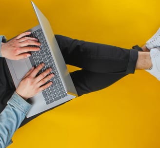 a man sitting on a yellow floor with a laptop on his outstretched legs