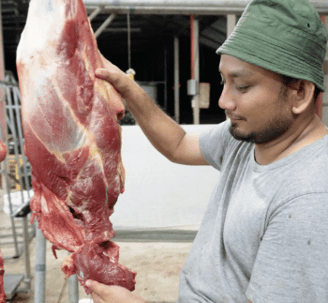 a man in a green hat and a large piece of meat on a table