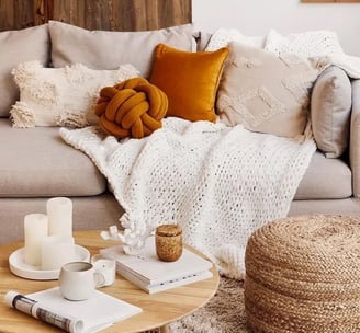 Couverture et coussins dans les tons beige et orange posés sur un canapé