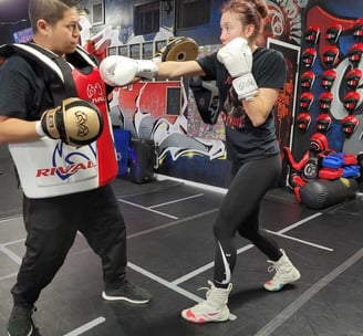 a woman in a boxing gloves is doing private boxing training with her coach