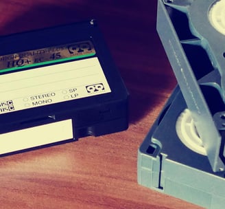 Three VHS tapes, partially out of frame on a tabletop, piled somewhat haphazardly/