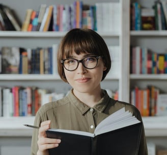 a woman in glasses and a green shirt is holding a book